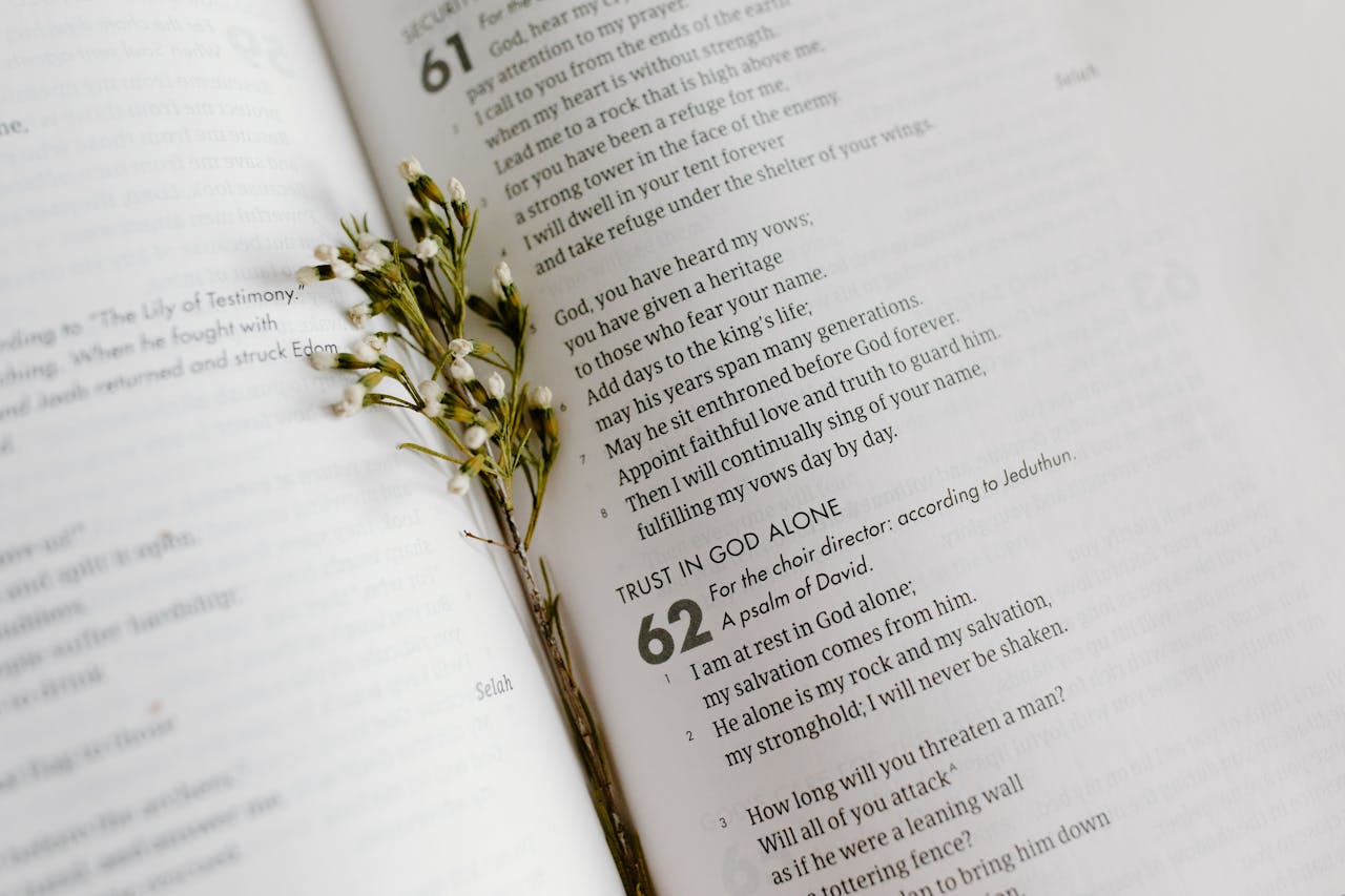 A close-up of an open Bible page with scripture and delicate white flowers.